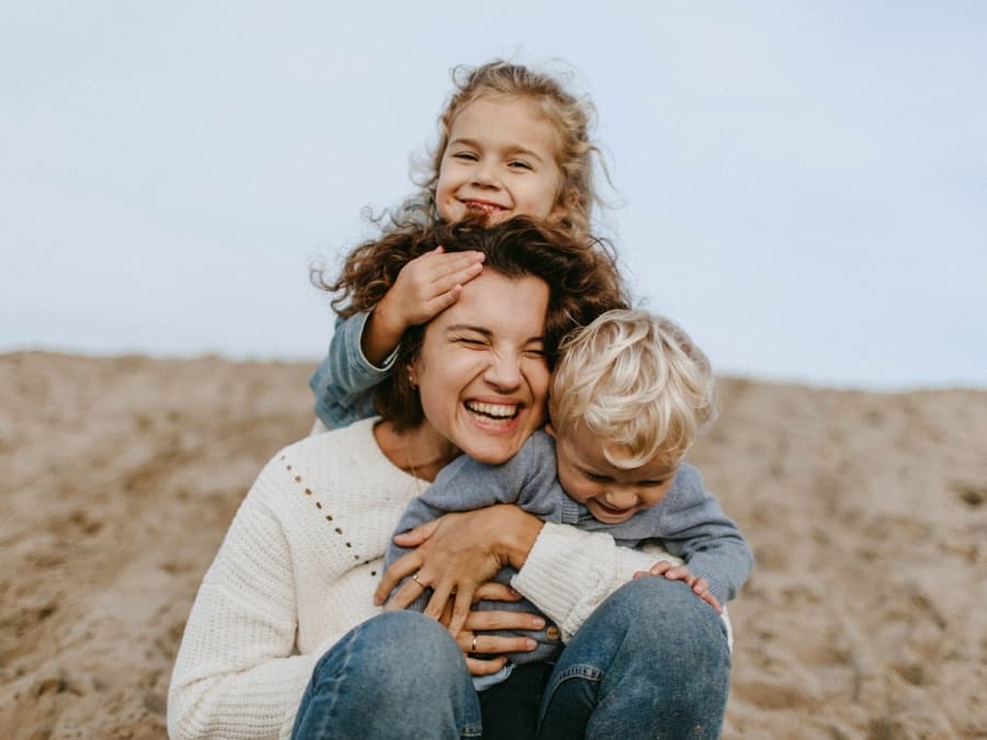 A mum laughing with her two children on a beach